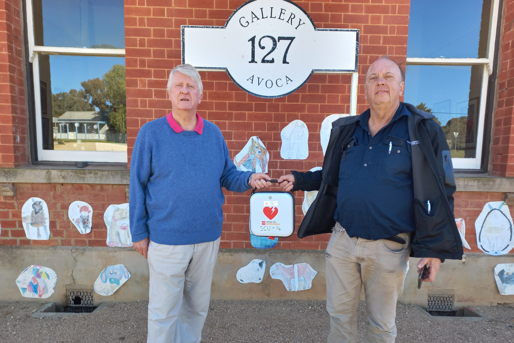 Murry Basin Rail Project representative Max Berry (right) hands over the new defibrillator to Gallery 127 Director Hugh Forster.