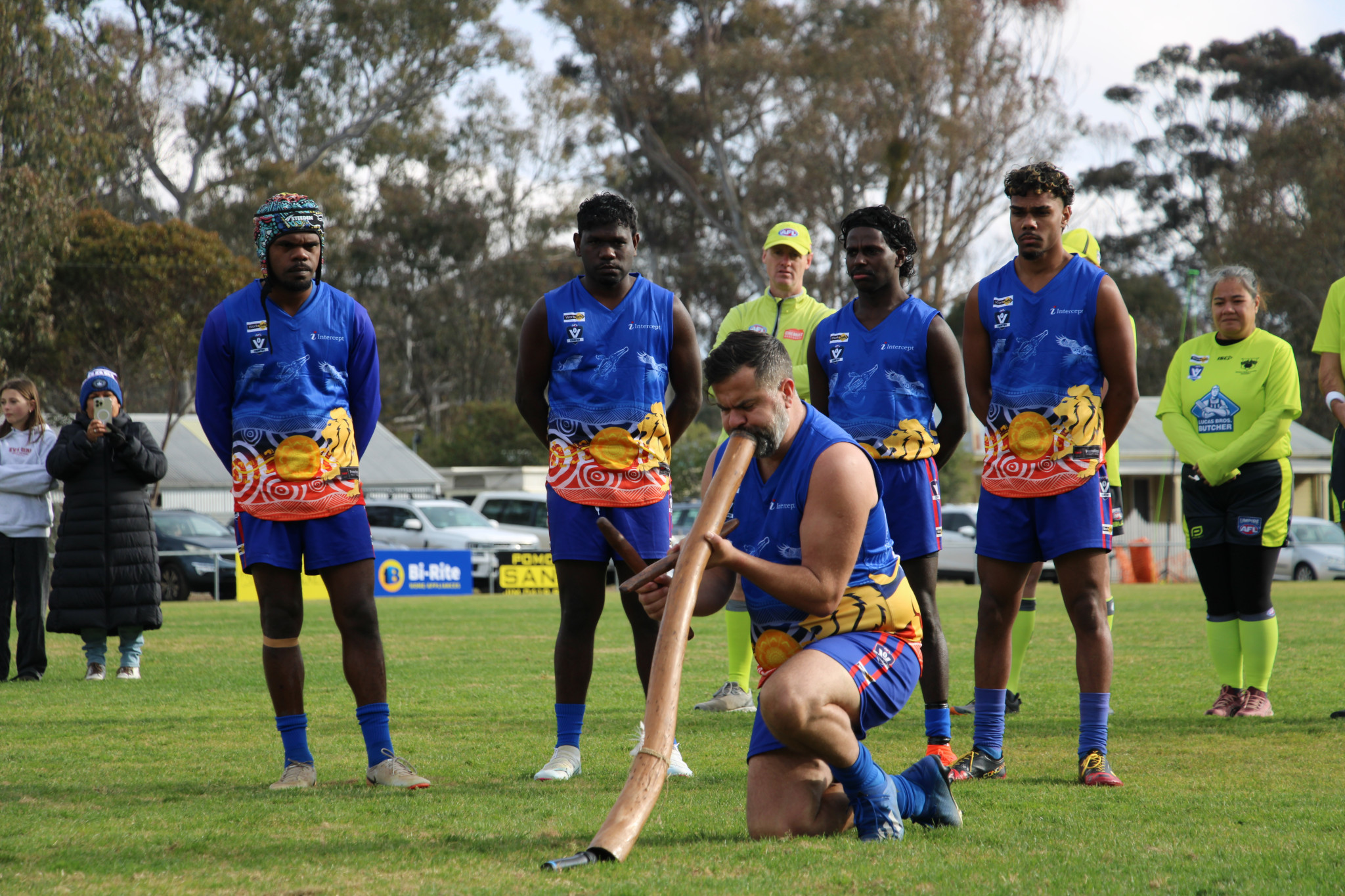 Kurt Dunn, Billy Munkara, Nate Cooper and Damien Dunn stand behind Paul Kelly as he is playing the Didgeridoo in the pre-game ceremony. PHOTO: ELLEN ANDERSON
